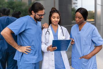 Multiracial diverse medical team in uniforms examining patient information on clipboard outdoors