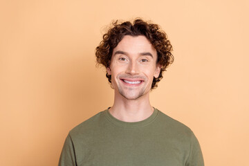 Portrait of a young man with curly hair in a khaki t-shirt against a beige background smiling...
