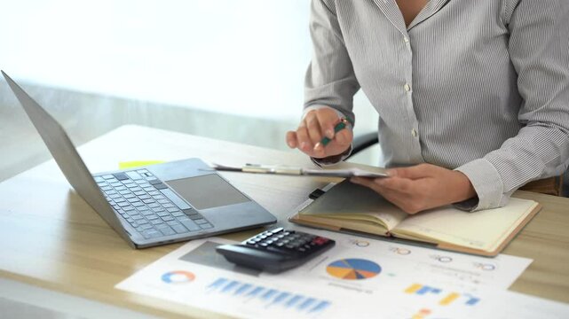 Business Financials: A focused individual meticulously reviews financial reports, surrounded by essential tools of the trade&mdash;a laptop, calculator.