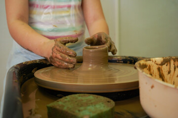 Child hands make earthenware cup working on pottery wheel at workshop.