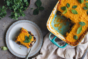 A baked casserole dish sits on a linen cloth, garnished with fresh mint. A slice is plated nearby with a fork. - Generative AI