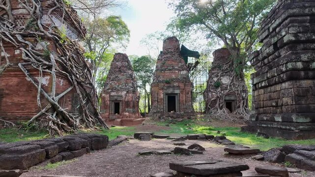 Wide shot frames all five stone towers of Prasat Bram, temple ruins glowing as sunlight filters through, casting a warm, golden glow over the ancient site.