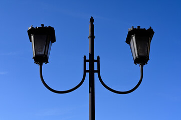 Two black street lamps and a blue sky