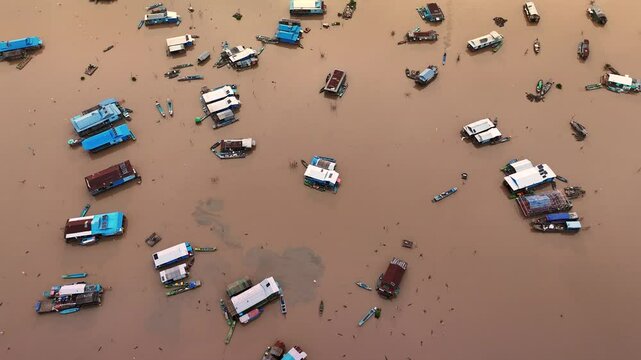 Top-down drone view of Tonle Sap&rsquo;s floating village, Cambodia, with floating houses and boats scattered across the murky lake.