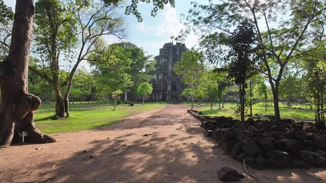 walkthrough shot moves along a path, framed by dense jungle, before unveiling the towering stone pyramid of Prasat Tom at Koh Ker, Cambodia.