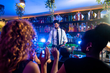 Bartender preparing cocktails in a trendy bar with clapping customers