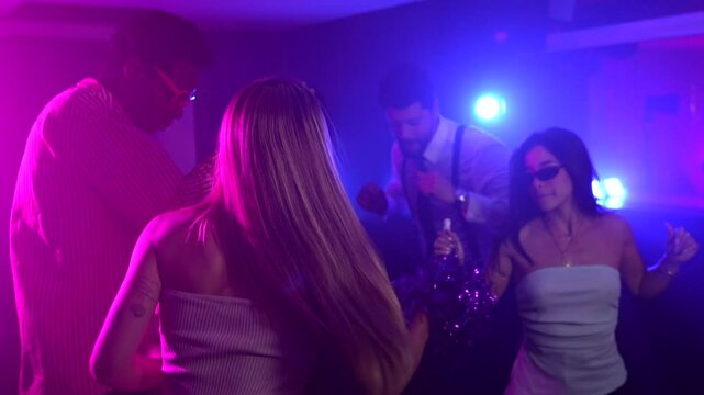 Young people enjoying nightlife, moving their bodies and waving pom poms under colorful lights