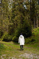 Adult in hooded raincoat explores lush conifer woods on winding path, evoking mindful escape, eco-travel and solitude; vertical frame leaves ample copy space above.