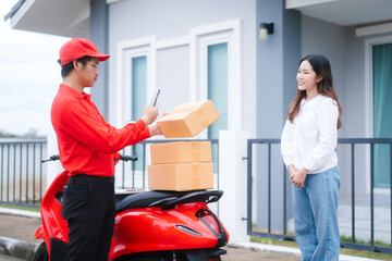 Attractive Asian delivery man in a red uniform hands a package to a middle-aged woman who is...