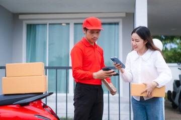 Attractive Asian delivery man in a red uniform hands a package to a middle-aged woman who is...