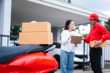 Attractive Asian delivery man in a red uniform hands a package to a middle-aged woman who is...