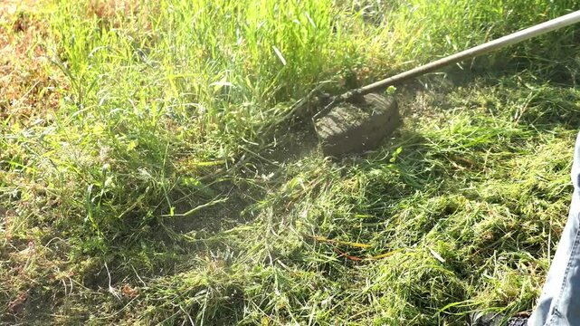 Trabalhador agr&iacute;cola de moto-ro&ccedil;adora no corte de erva densa. Servi&ccedil;o de ro&ccedil;agem em zona rural com ferramenta motorizada