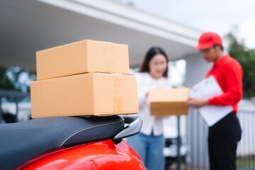Attractive Asian delivery man in a red uniform hands a package to a middle-aged woman who is...
