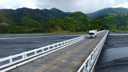 Truck driving on bridge over river in hilly area. Top view of truck driving over concrete bridge...