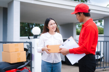 Attractive Asian delivery man in a red uniform hands a package to a middle-aged woman who is...