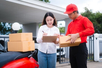 Attractive Asian delivery man in a red uniform hands a package to a middle-aged woman who is...