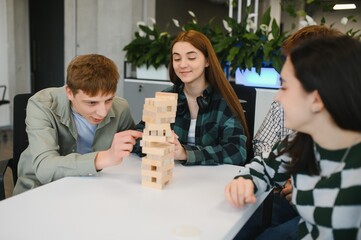 Young office workers playing wooden block tower game at desk