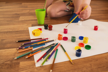 boy child preschooler, draws with gouache paints and pencil on sheets of paper while sitting on the...
