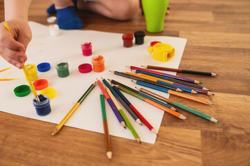 boy child preschooler, draws with gouache paints and pencil on sheets of paper while sitting on the...