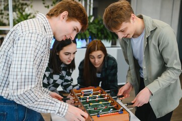 Young coworkers playing table football in office break room