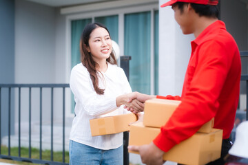 Obraz premium A delivery man, who appears to be Asian, in a red uniform shakes hands with a smiling woman, who seems to be middle-aged and holding a package, at the entrance of a modern home.
