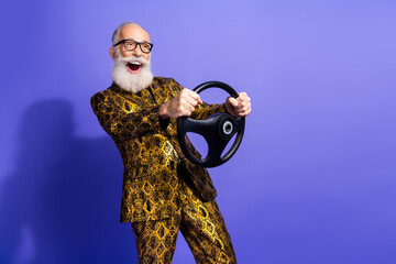 Vibrant elderly gentleman in a stylish patterned suit joyfully holding a steering wheel against a...