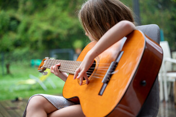 Young girl playing acoustic guitar on terrace with green nature background