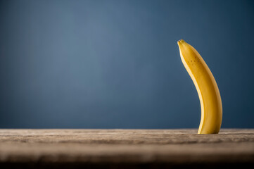 Single banana standing upright on wooden table with blue background