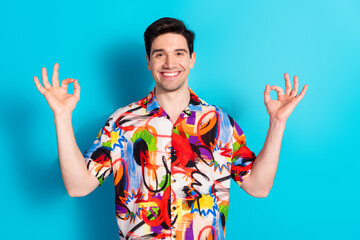 Young man in colorful shirt on blue background showing hand gestures and smiling joyfully...