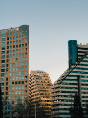 Fototapeta premium Contemporary architecture showcasing residential and commercial buildings against clear sky, bathed in warm glow of setting sun in Madrid, Spain. Modern architectural skyline, residential structures