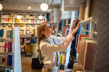 Woman selects books in bookstore alone. Female book lover browsing, searching textbooks, handbooks,...