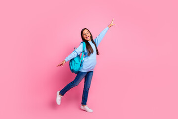 Cheerful young girl in casual outfit posing joyfully against pink background, wearing a backpack...