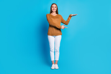 Smiling young woman in casual outfit making presentation gesture against blue background