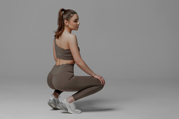 Model poses in athletic wear showcasing a squat exercise in a minimalist studio setting with gray...