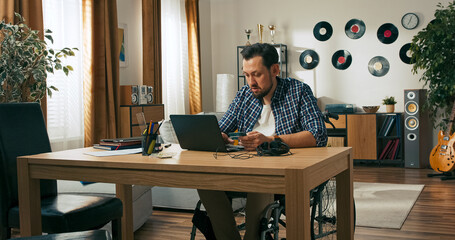 A bearded man who uses a wheelchair finishes his freelance work at home with a smile. He closes his laptop, places a credit card on the table, and enjoys the ease of online payment.