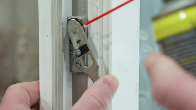 A hand lubricates a door mechanism with a spray can, ensuring smooth door operation