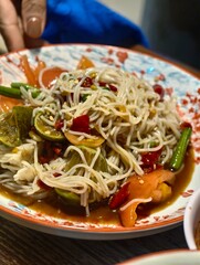 Colorful Asian Noodle Dish with Vegetables and Spicy Sauce on Decorative Plate Garnished with Fresh Herbs