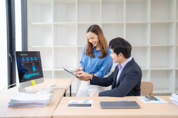 Two young professionals collaborating on a project, analyzing financial data on a tablet and desktop in a modern office, exemplifying teamwork and data-driven decision-making