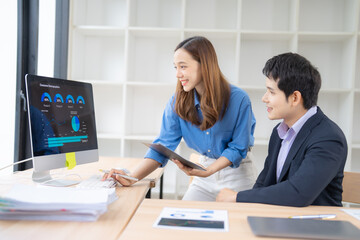 Two business professionals engage in data analysis, using a desktop computer and a tablet. They collaborate in a modern office environment with charts and graphs displayed on the screen