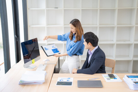 Two business professionals collaborate in a modern office, analyzing financial data on a digital tablet and desktop computer. Charts and graphs are visible, indicating a focus on growth