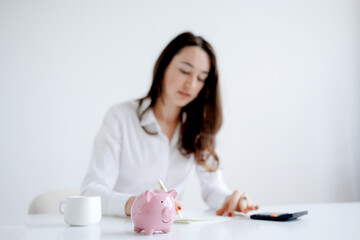 Woman managing finances at a white desk with a piggy bank and calculator in a bright and minimal workspace