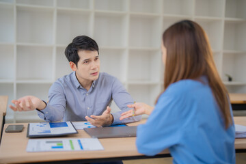 Two southeast asian marketing professionals sitting at a desk in a modern office, analyzing and discussing disappointing statistics of a new project, trying to understand the causes