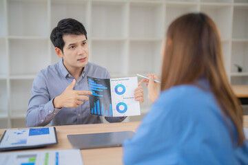 Two business professionals engaged in a discussion, analyzing financial charts and graphs. They are focused on interpreting data and making strategic decisions in an office setting