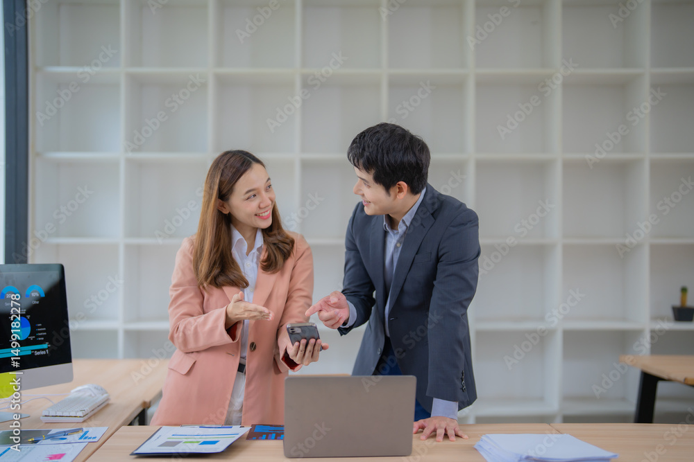 Poster two asian businesspeople discussing over a smartphone in a modern office, collaborating on a project