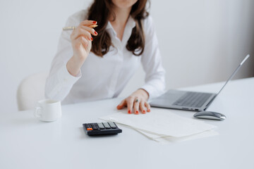 Person working at a desk with a laptop, calculator, and paperwork during daytime in a modern office...