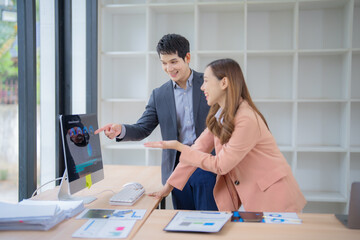 Two Asian business professionals collaborating in an office, discussing marketing data on a...