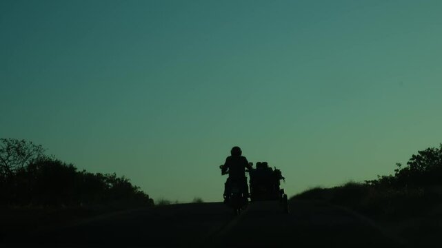a farmer moving in silhouette at sunrise on a motorcycle with a sidecar
