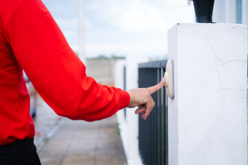 A hand presses the button of a modern doorbell mounted on a white pillar, possibly initiating a...