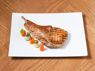 Grilled pork chop with spicy Thai dipping sauce and vegetable garnish on white plate