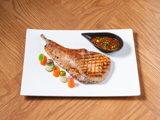 Grilled pork chop with spicy Thai dipping sauce and vegetable garnish on white plate
